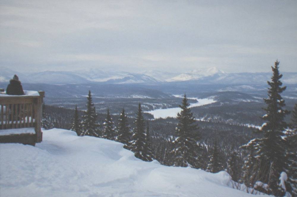 A snowy hilltop clearing with a distant view toward mountains in pale winter light