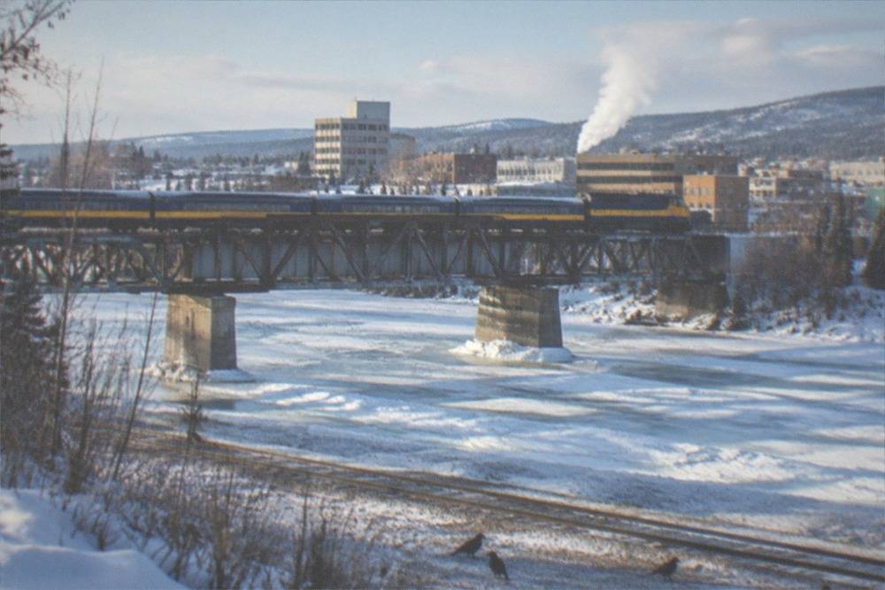 A passenger train crossing a snowy Interior Alaska landscape beside a frozen river