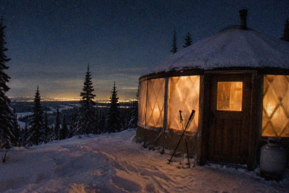 A heated yurt with large windows glowing under a starry night sky outside Fairbanks