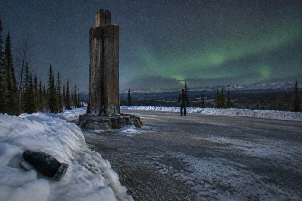 A wooden roadside sign marking the Arctic Circle beside a snowbank under a dark starry sky