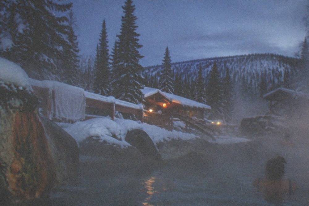 Steam rising from an outdoor hot springs pool surrounded by deep snow under a night sky