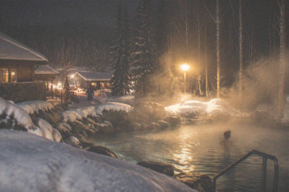 A steaming outdoor hot spring pool surrounded by snow at night