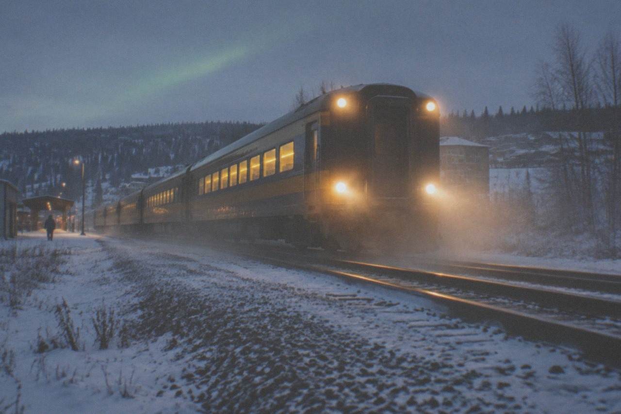 A passenger train winding through snowy Alaska wilderness under a dark evening sky