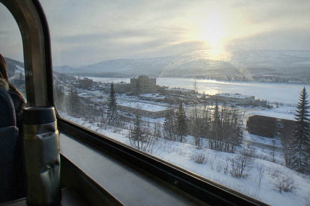 A train window view of wide snowfields with mountain ridges fading into winter haze.