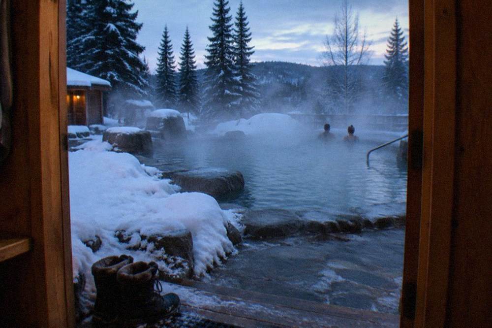 Steam rising from an outdoor hot springs pool surrounded by snow at dusk.