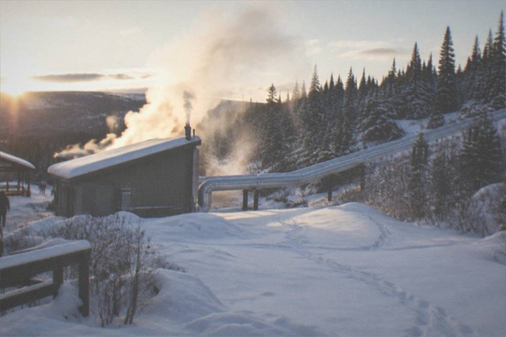 A small geothermal power plant with pipes beside a snowy forest clearing.