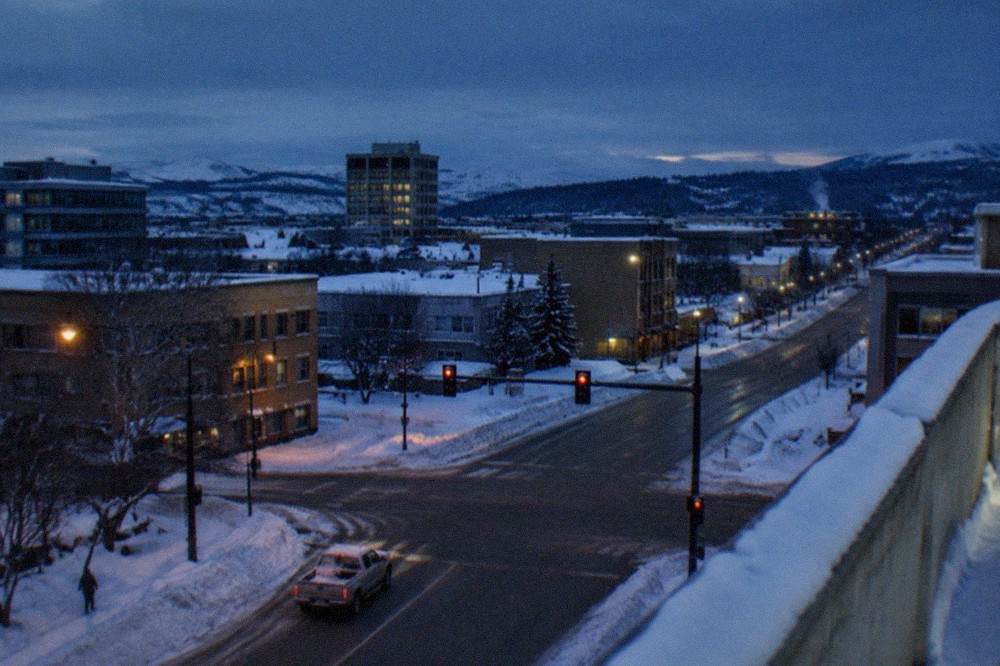Downtown buildings under deep blue twilight with snow banks along the roadside