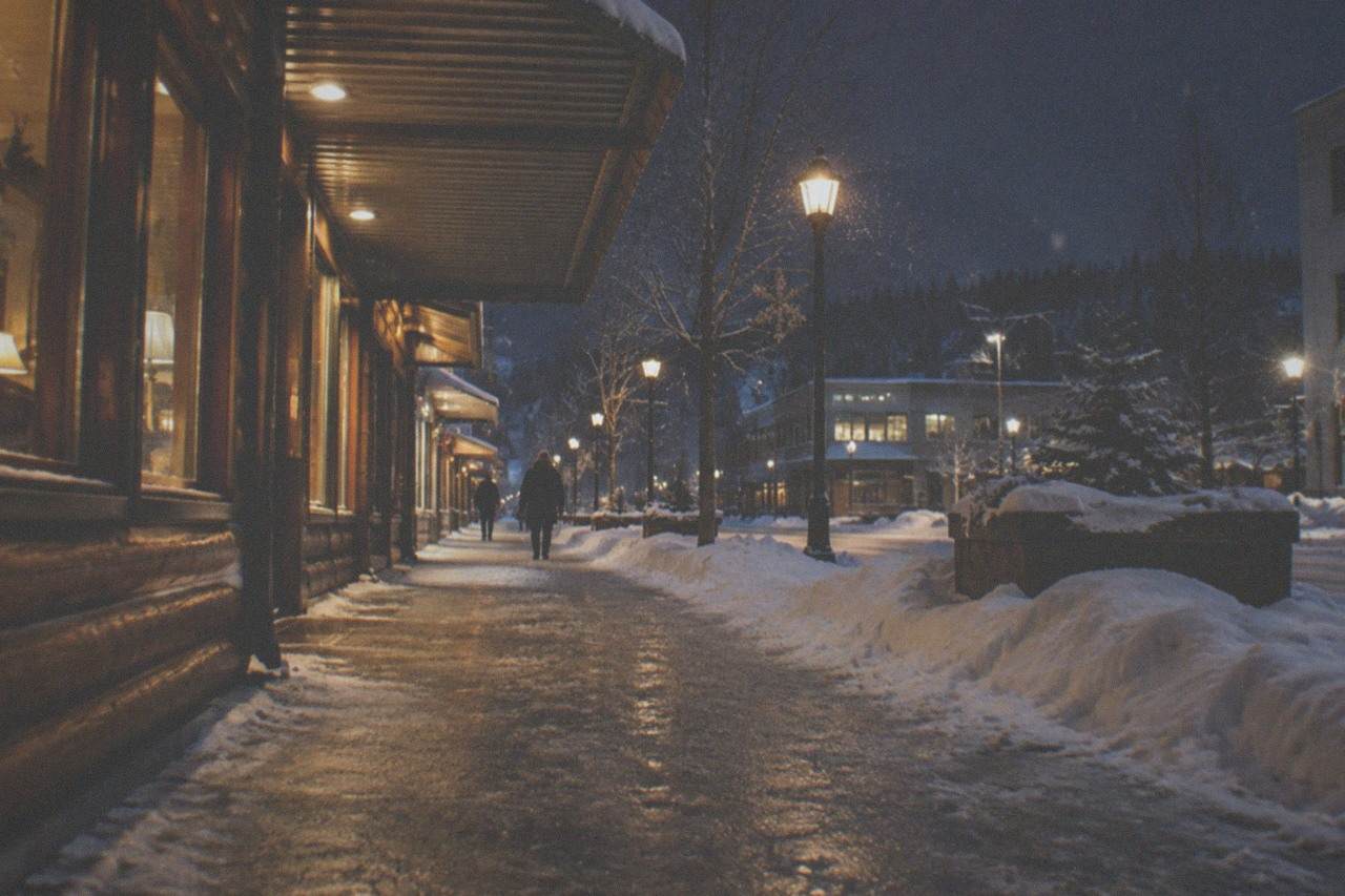 Snow-covered street with warm lit storefronts under a dark winter sky in an Interior Alaska city