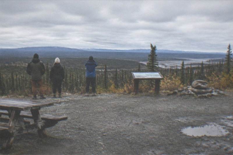 A tour group posing at the Arctic Circle marker sign along the Dalton Highway