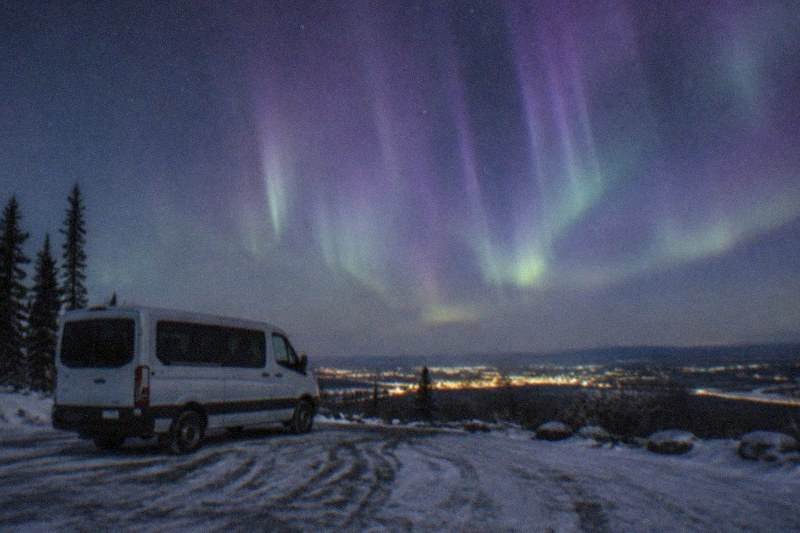 A small tour van parked on a dark roadside outside Fairbanks, Alaska, waiting under the aurora