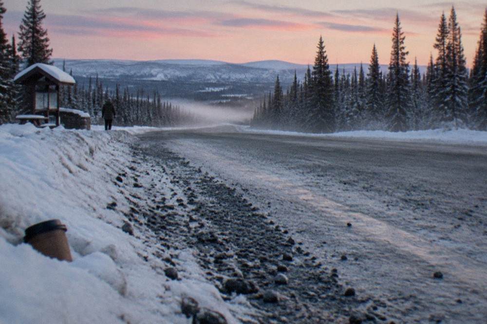 A gravel highway cutting through snowy boreal forest under a wide twilight sky