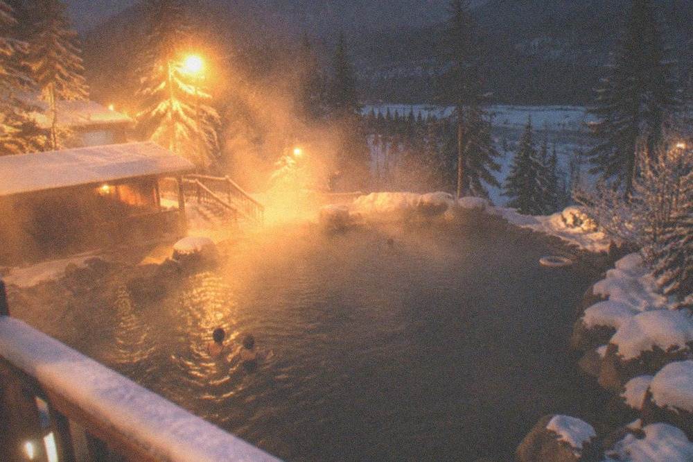 Steam rising from an outdoor hot springs pool surrounded by snow at night