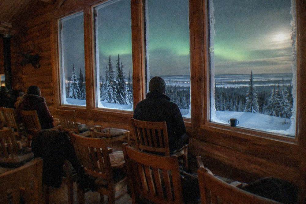 Wooden lodge interior with rows of chairs facing tall windows onto a dark snowy landscape