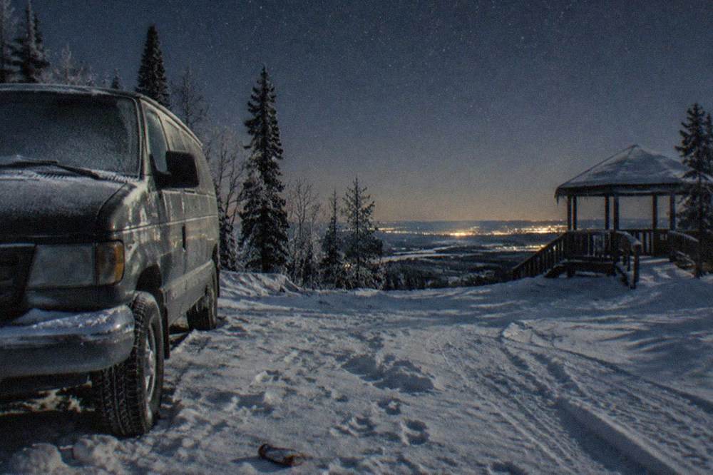 A parked tour van at a snowy Murphy Dome hilltop clearing under a starry night sky