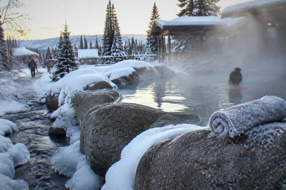 Steam rising from an outdoor hot springs pool surrounded by snow at a resort