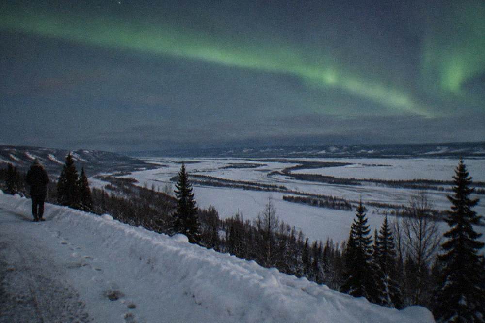 A calm display of pale green light stretched across a dark sky above a flat snowy landscape