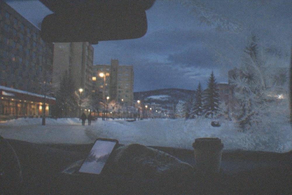 A forecast screen glow lighting a person's mittened hand, no people visible, above a frost-covered car window at night