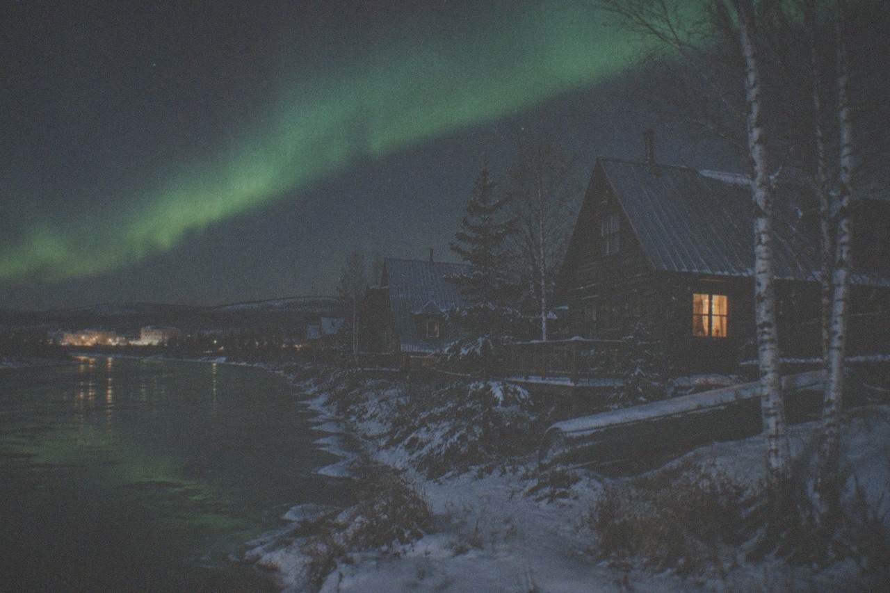 A green aurora band arcing over a snowy forest clearing under a starry night sky