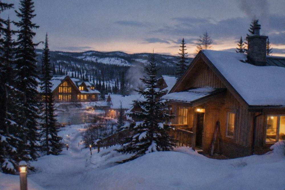 Snow-covered resort buildings lit warmly against a dark forested valley