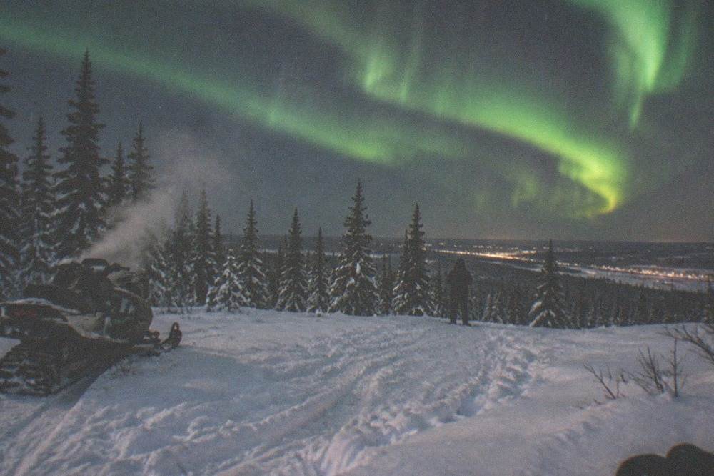 Green aurora bands above a snowy forest clearing with faint steam drifting