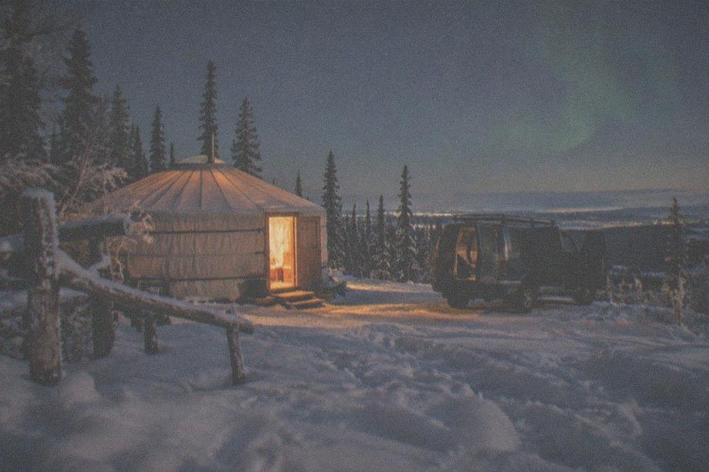 A heated yurt glowing on a dark hillside with a vehicle waiting outside