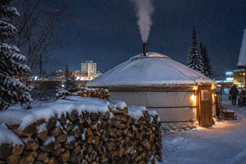 A wood-heated yurt glowing warmly from inside on a dark snowy evening