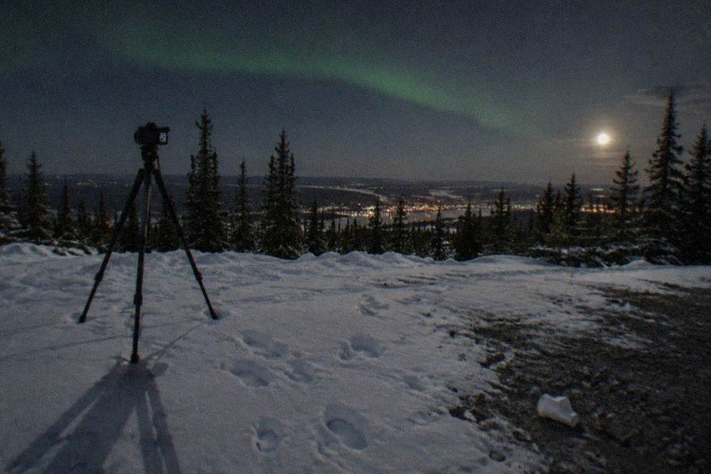 A camera on a tripod pointed at a starry sky above a snowy clearing