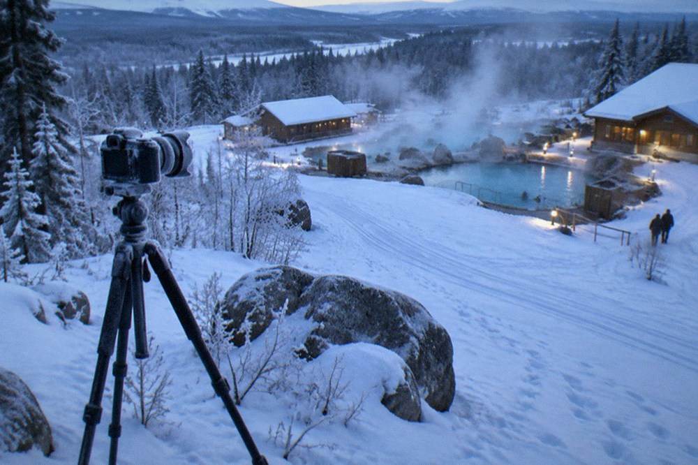 A wide camera lens resting on a tripod in blue twilight over snow