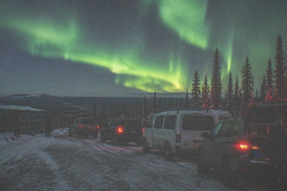 A small group of parked vehicles on a snow-covered road under a bright aurora