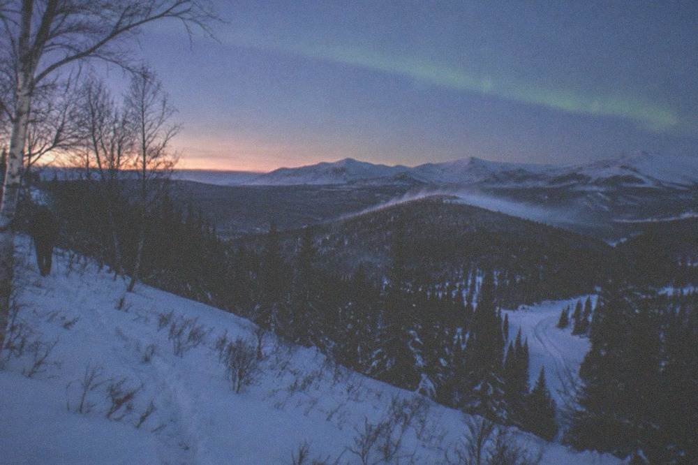 Snow-covered hills under a deep blue twilight with a faint aurora band