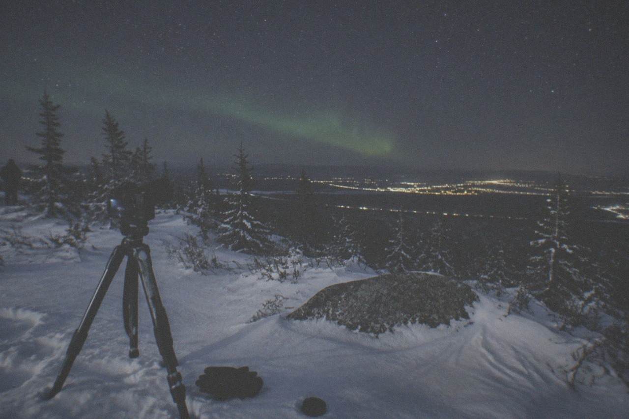 A camera on a tripod pointed at a starry sky above a snowy clearing