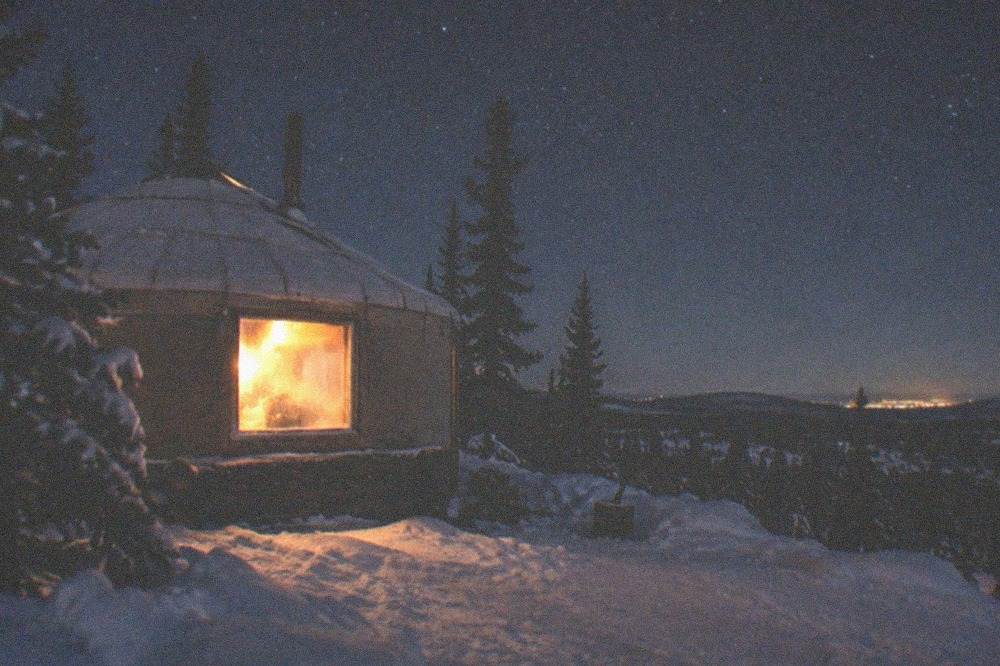 A heated aurora viewing yurt with warm light in the window under a starry night sky