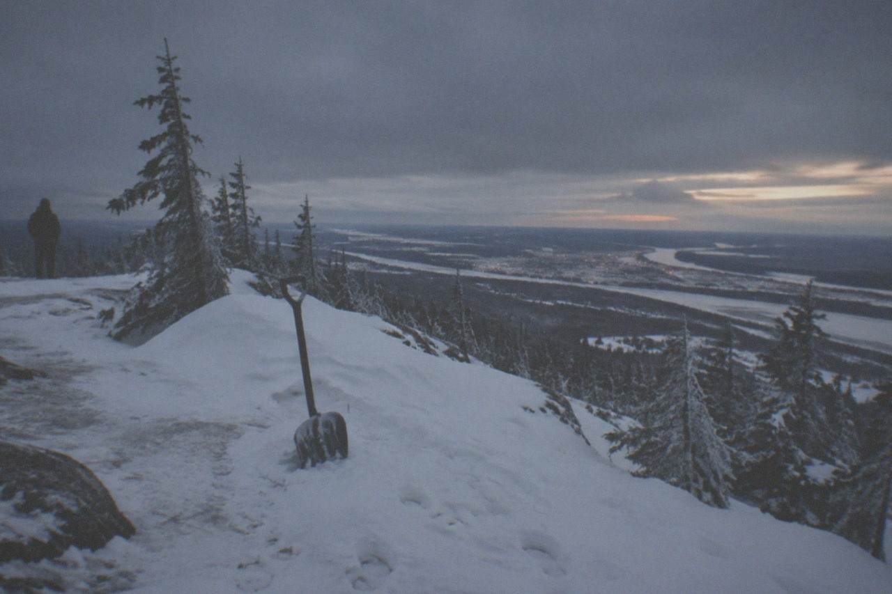 Snow-covered hilltop viewing area under a heavy low cloud bank at dusk near Fairbanks