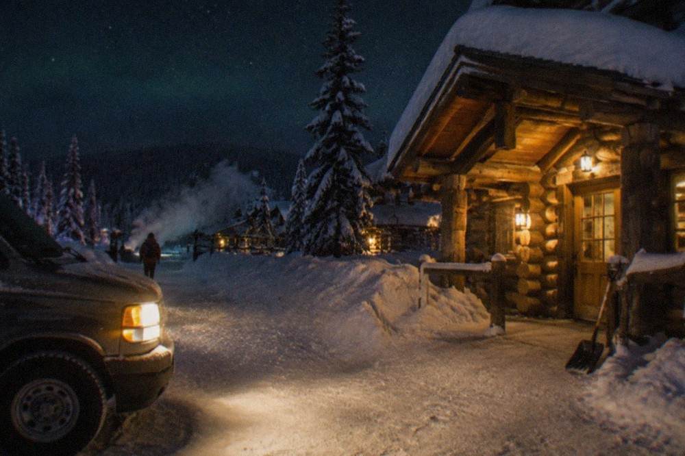 A heated van parked at a snowy lodge entrance under a starry night sky