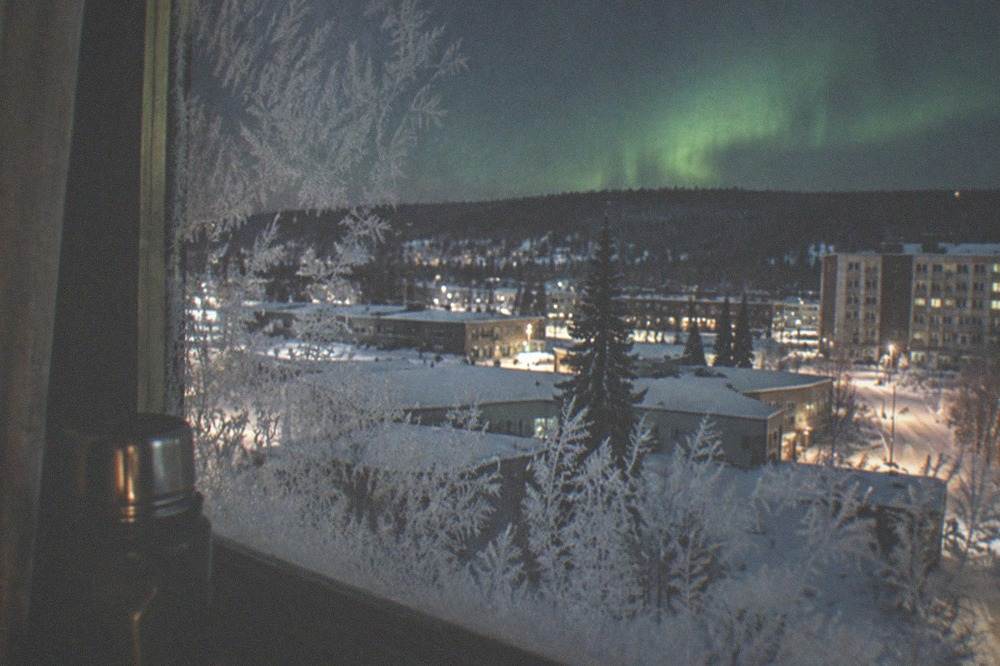 Frost-covered window glass at night with a dark sky and faint aurora glow beyond