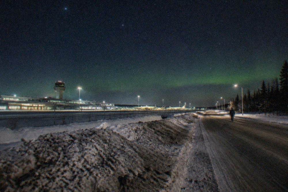 A winter road in interior Alaska under a starry sky with a faint green glow on the horizon