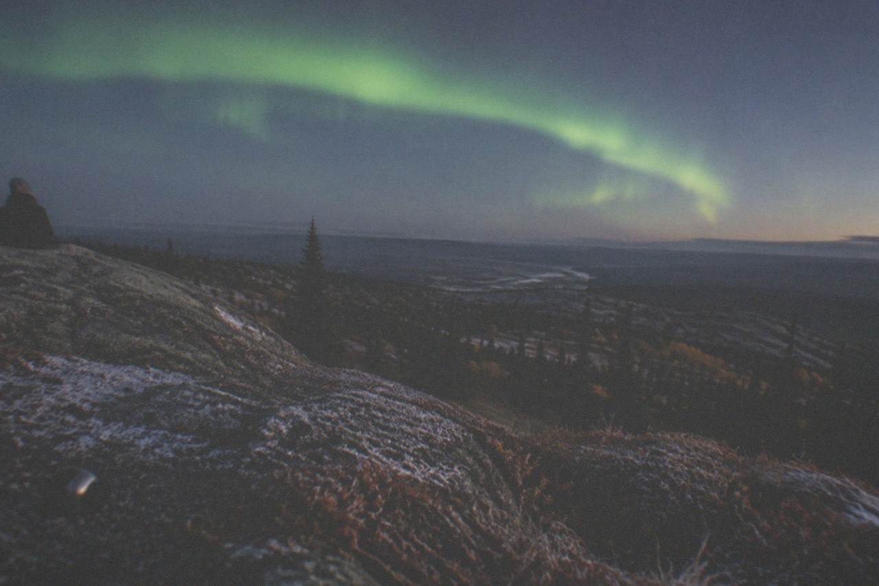A green aurora band arcing over a dark forested ridge in interior Alaska
