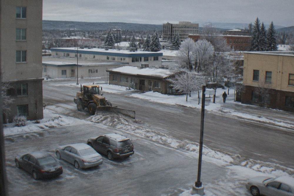 Snow-covered street with parked cars and a layer of ice under a gray winter sky