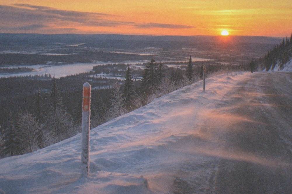 Winter road sign partly drifted with snow under a low evening sky
