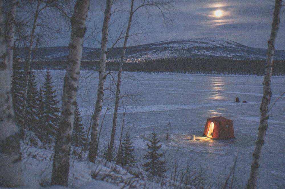 Warm light spilling from a heated ice fishing shelter onto a frozen lake at night