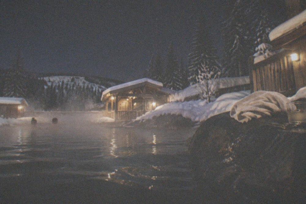 Steam rising from an outdoor hot springs pool surrounded by snow under a starry night sky