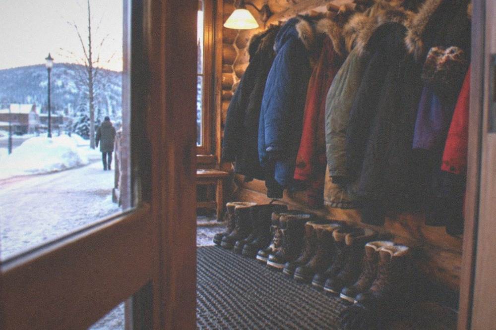 Winter coats and insulated boots lined up inside a warm wooden lodge entryway