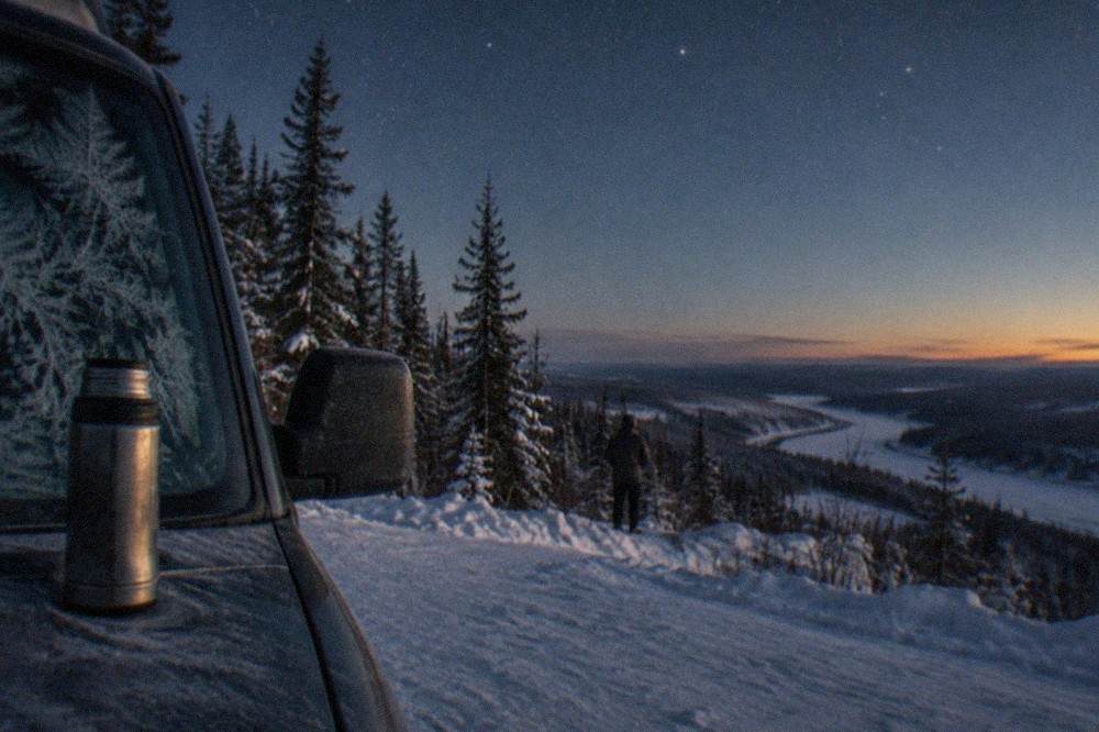 A heated van parked on a snowy roadside at night with headlights off and stars overhead