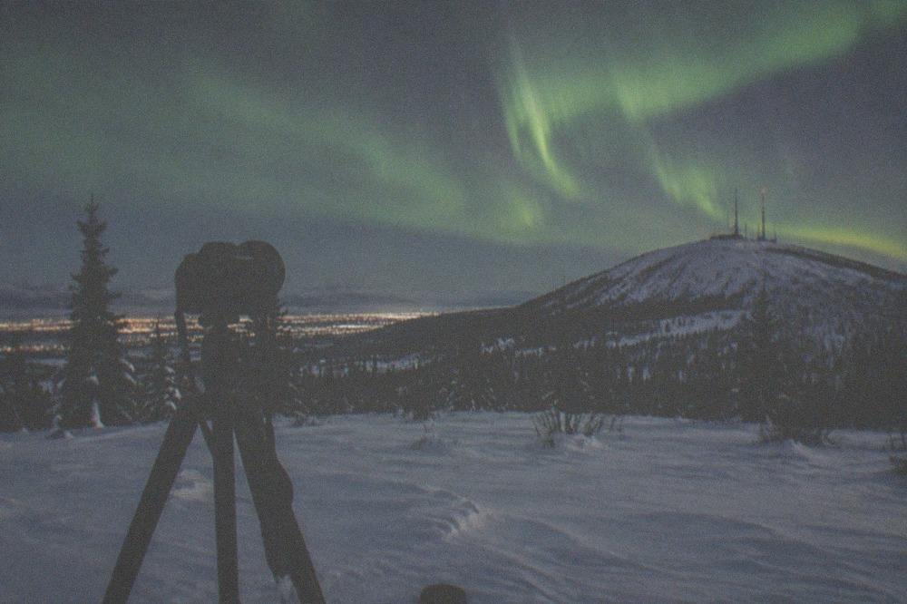 Aurora over a frozen field with a camera tripod silhouette in the foreground