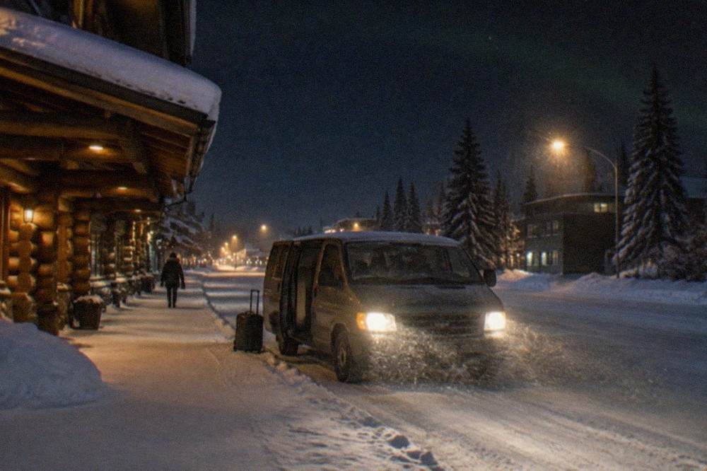 A parked van with headlights on beside a snowy road at the edge of Fairbanks under a starry sky