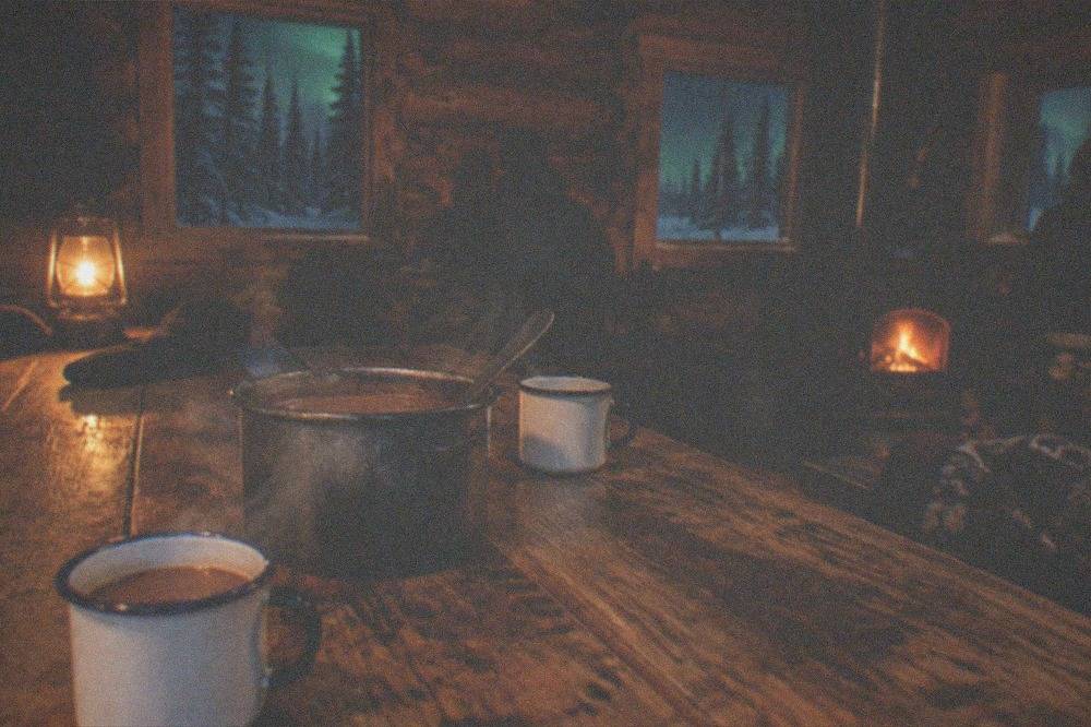 Steam rising from cups of hot drinks on a wooden table inside a warm aurora viewing shelter at night