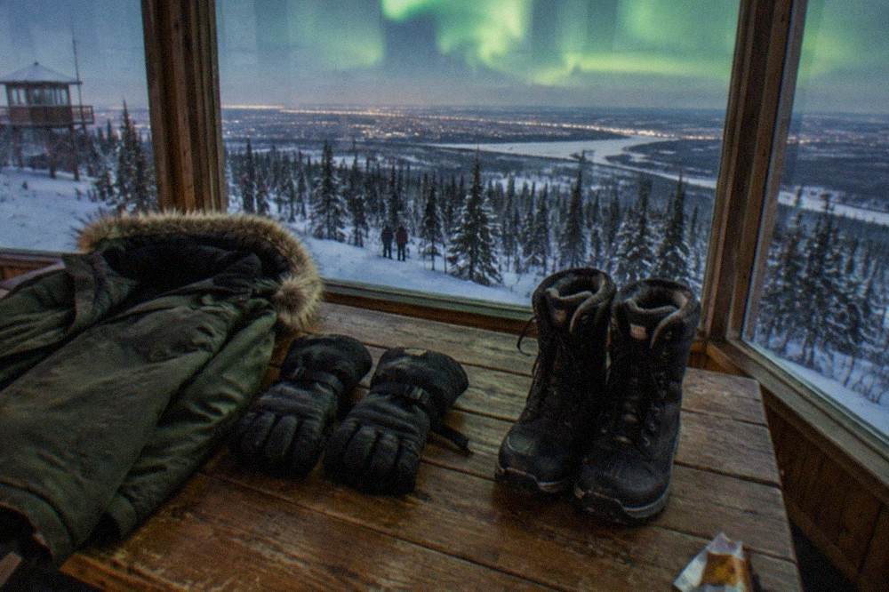 A parka, insulated gloves and winter boots laid out on a wooden table