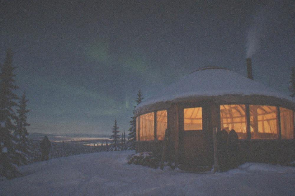A warmly lit wooden yurt under a starry winter sky in Alaska