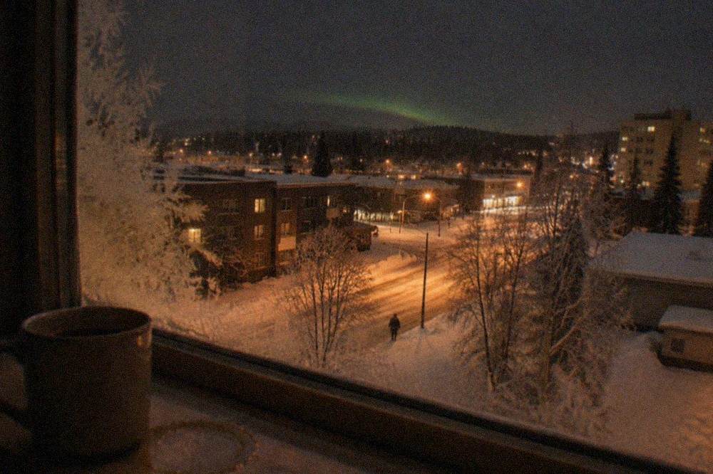 A hotel window in Fairbanks with faint green glow on the horizon beyond streetlights