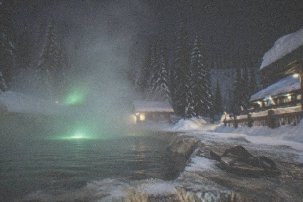 Steam rising from an outdoor hot springs pool surrounded by snow and dark forest at night